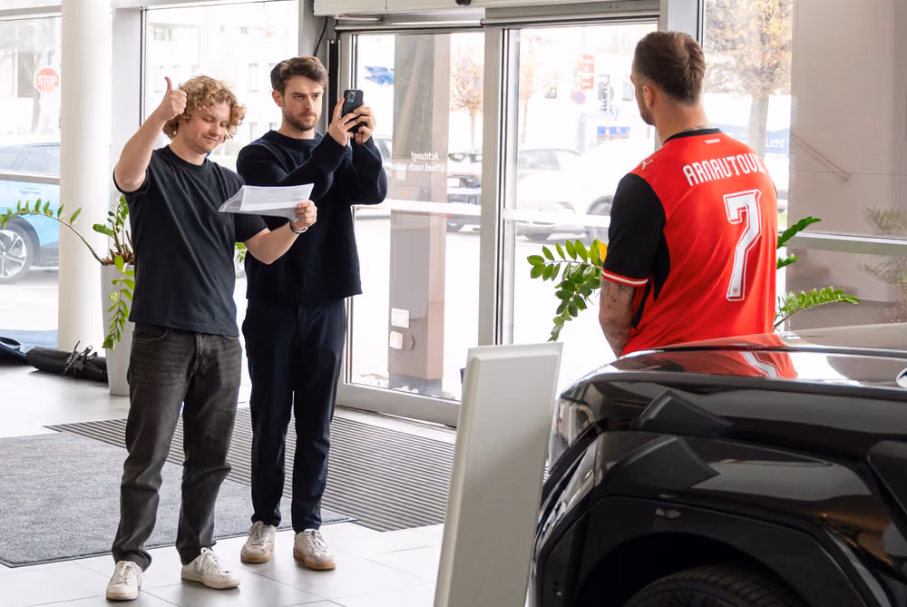 Zwei Teammitglieder filmen im Autohaus, Marko Arnautović steht neben einem schwarzen Hyundai